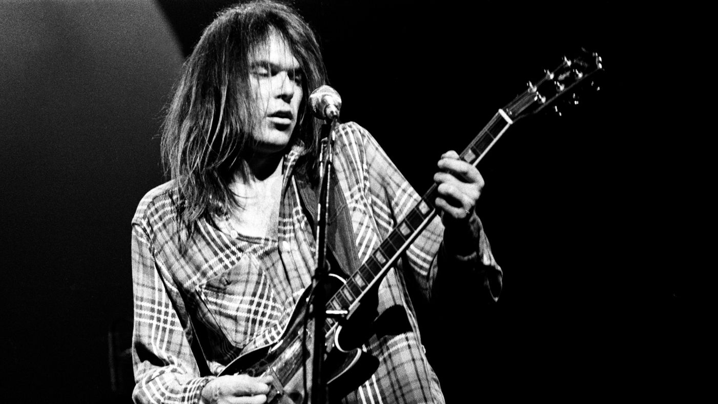 Neil Young, ícone do rock, exibe maestria com sua guitarra, personificando o legado musical duradouro. Sua expressão artística única ecoa em cada nota, eternizando sua influência na história da música.