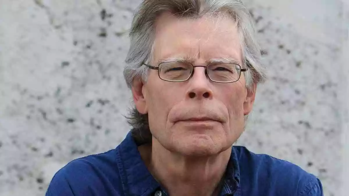 Foto de Stephen King sentado, cercado por livros e manuscritos, refletindo a profundidade de sua obra literária em terror e fantasia.