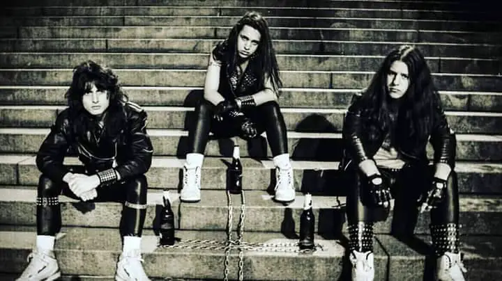 Foto da banda brasileira de speed metal Álcool, um trio sentado em uma escada, exibindo uma vibe de metal underground.